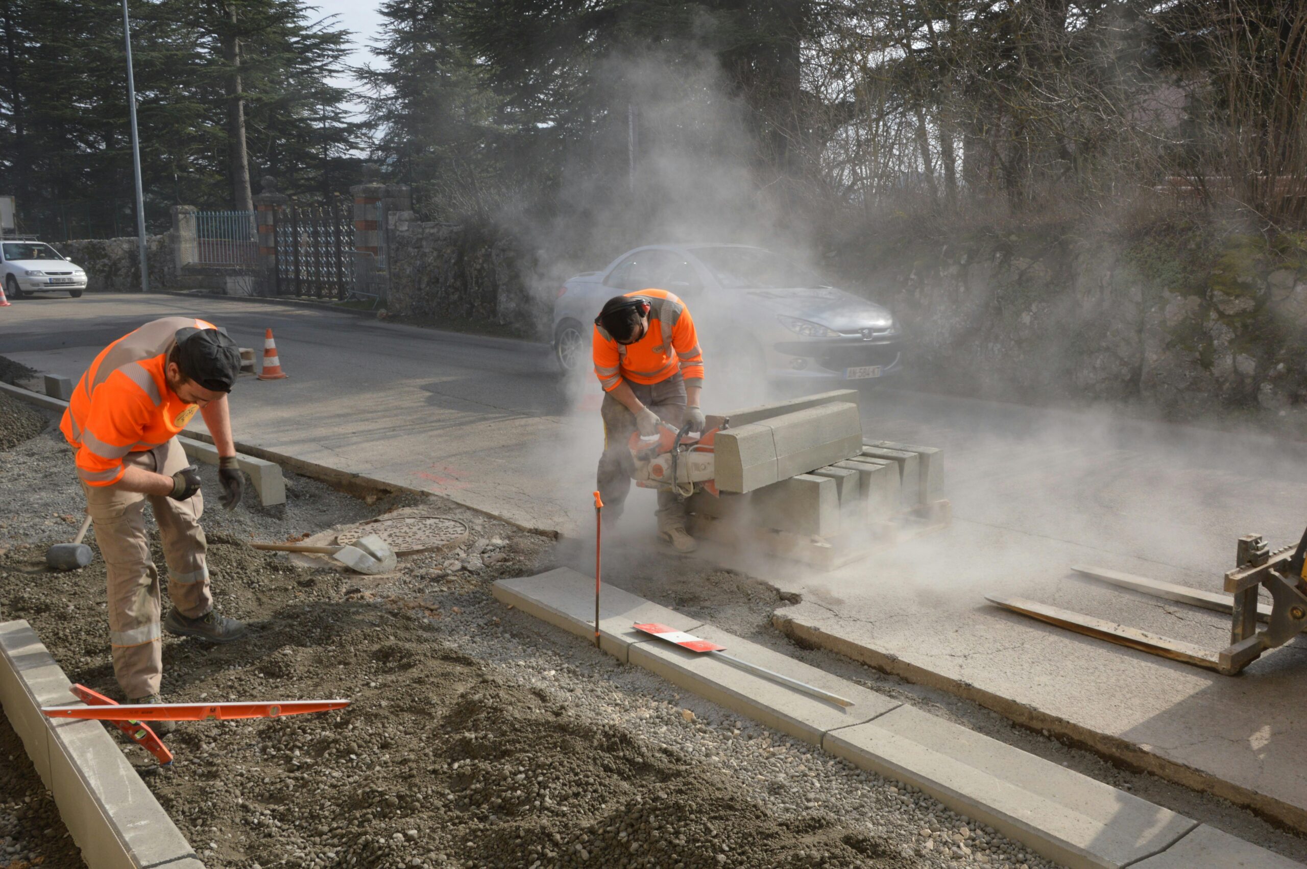 Workers cutting concrete on a road with a chainsaw, creating dust and working efficiently.