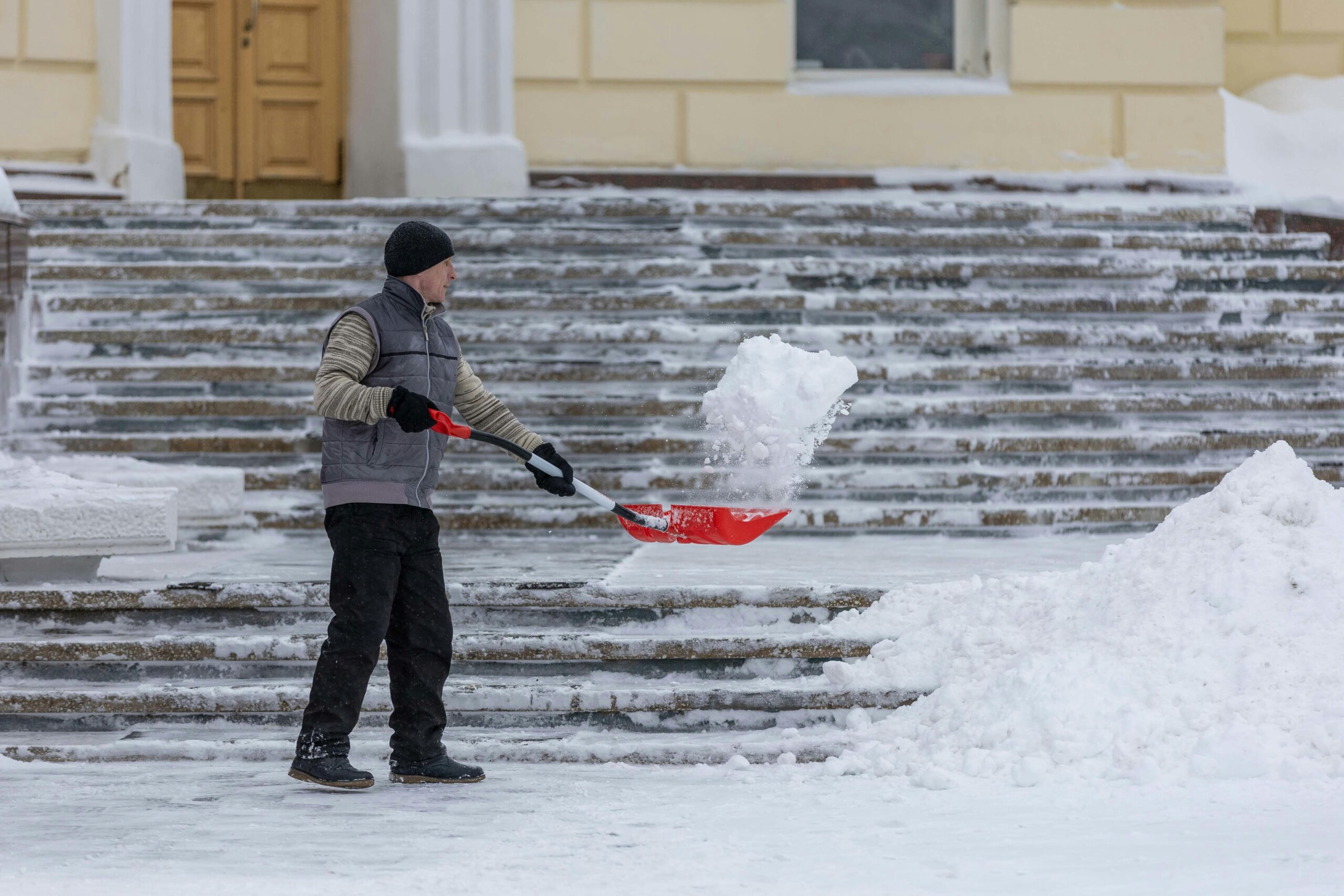 A man clearing snow and ice from outdoor steps during a winter snowstorm.